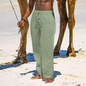 Detailed view of men's loose cotton linen wide leg casual pants in sage green on beach.