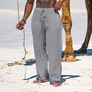 Close-up of men's loose linen trousers with drawstring waist shown in a tropical beach scene.
