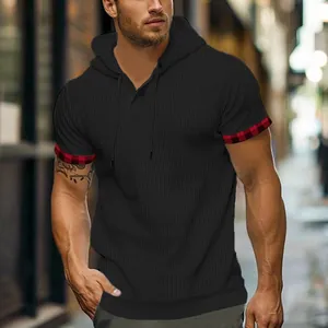 Dettaglio di t-shirt nera con cappuccio in maglia a nido d'ape e polsini a quadri rossi