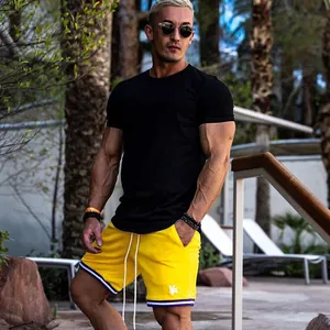 Man in muscular fit black gym t-shirt and yellow athletic training shorts outdoors
