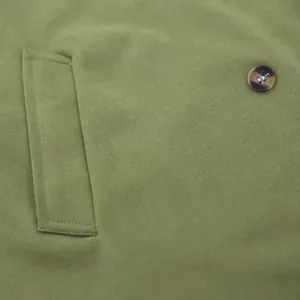 Close-up of green casual jacket fabric featuring a brown button and stitched pocket detail.