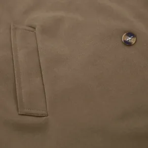 Close-up of brown men's trench coat detail featuring a marbled button and pocket stitching.