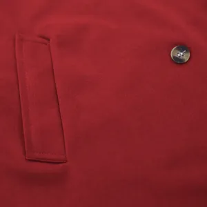 Close-up of red trench coat fabric showing pocket flap and marble pattern button detail.
