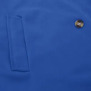 Macro detail of a blue men's trench coat highlighting the side pocket and button texture.