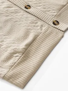 Macro detail of beige men's cardigan featuring jacquard knit texture and marbled buttons.