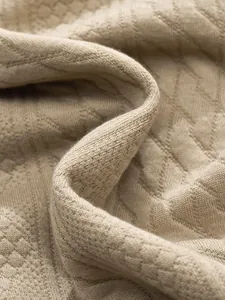 Close-up macro detail of beige jacquard knit fabric showing intricate geometric patterns.