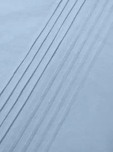 Macro view of pleated fabric detail on light blue linen long sleeve Henley shirt