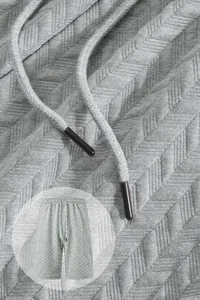 Detail view of grey jacquard shorts fabric with textured chevron pattern and drawstring