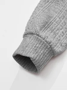 Macro view of a grey cardigan sleeve showing textured jacquard fabric and ribbed cuff detail.