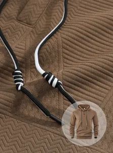Détail du sweat à capuche marron montrant le tissu jacquard et les cordons bicolores.
