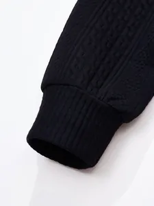 Close-up detail of black knitted cardigan sleeve showing ribbed cuff and jacquard pattern