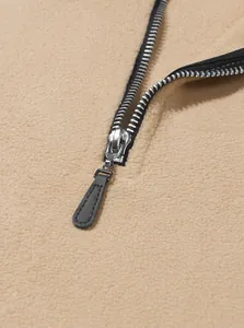 Detailaufnahme von schwarzem Reißverschluss und weicher Fleece-Textur des beigen Sweatshirts