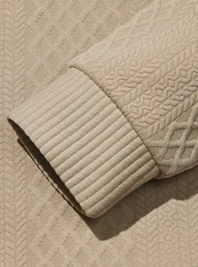 Close-up of men's beige sweatshirt showing heavy jacquard fabric texture and ribbed cuff detail.