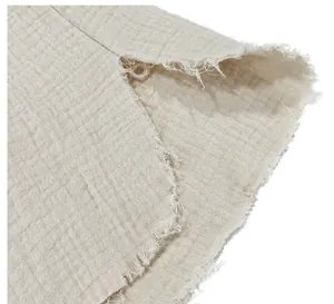 Close-up detail of distressed frayed edges on a light beige cotton muslin shirt.
