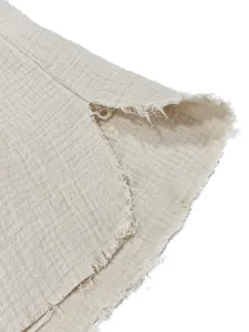 Detailed view of distressed frayed hem on men's cream textured cotton shirt