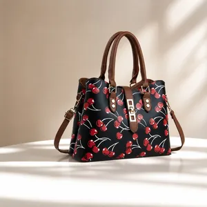 Vista detallada de un bolso de moda con patrón de cerezas y asas marrones y cierre dorado