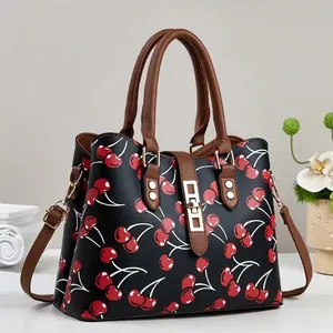 Close-up of stylish black handbag featuring red cherry print and brown handles.