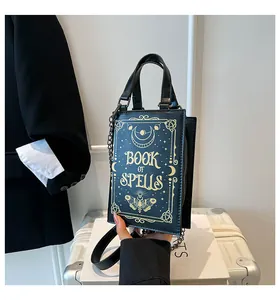 Detail of a creative black book-shaped crossbody bag with 'Book of Spells' gold print.