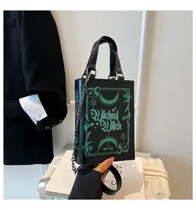 Detail shot of a black book-shaped handbag with green Wicked Witch print and chain strap