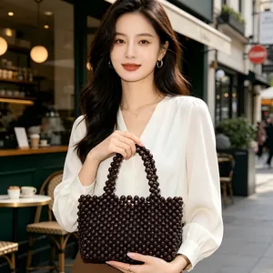Borsa fatta a mano in perline di legno tenuta da una modella in un elegante caffè