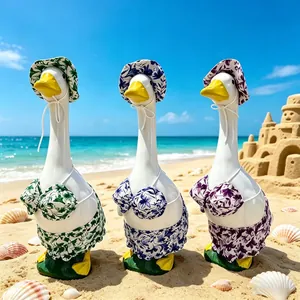 Detail of three garden goose figurines wearing colorful floral bikini beach outfits on sand