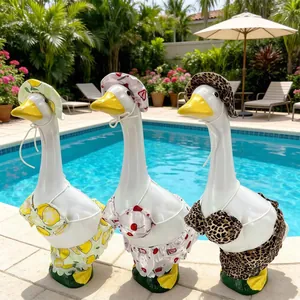 Detail of three garden goose statues wearing summer bikini and hat sets by the pool.