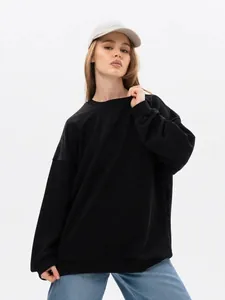 Oversized black crewneck sweatshirt paired with jeans and a grey cap for a street style look