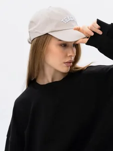 Detail view of a minimalist black crew neck sweatshirt worn by a model with a baseball cap