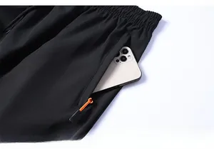 Dettaglio della tasca con cerniera sicura su pantaloncini sportivi neri con linguetta arancione