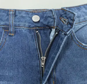 Vue détaillée de la fermeture éclair métallique et du bouton sur un jean délavé bleu