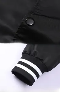 Detail van een zwart varsityjack met drukknoop en gestreepte geribbelde manchetten