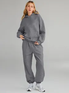 Full body shot of a woman wearing a loose gray hooded tracksuit with white sneakers