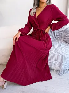 Close-up view of a burgundy pleated maxi dress with V-neck and tie waist on a white sofa