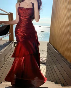 Shimmering red mermaid dress with ruffled hem shown on a model at a beach sunset.