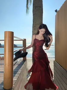 Full view of a shimmering red mermaid ruffle dress worn by a model on a tropical beach.