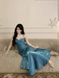 Elegant metallic blue mermaid evening gown with ruffled details worn by model on sofa