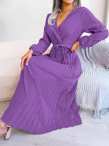 Full view of elegant purple V-neck pleated maxi dress shown on a model sitting on a sofa.