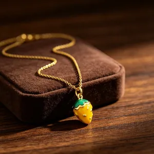 Close-up of a sweet yellow strawberry enamel pendant on a gold-plated necklace chain