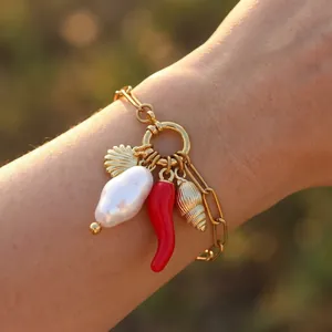 Detail view of gold chain bracelet with baroque pearl, red chili, and shell charms.