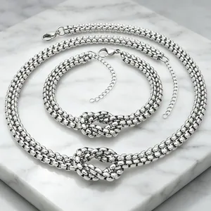 Close-up detail of chunky stainless steel knotted necklace and bracelet set on marble.