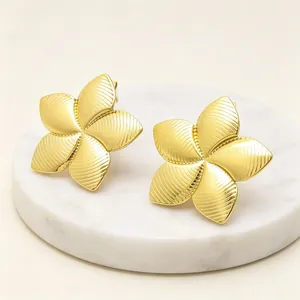 Macro detail of elegant gold-toned flower earrings with textured petals on marble base