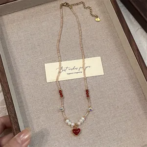 Close-up detail of a beaded necklace with a red heart pendant and pearls on a tray
