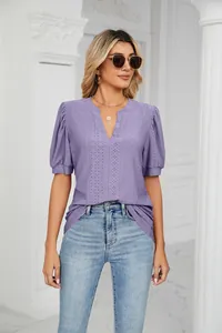 Woman wearing a purple eyelet v-neck puff sleeve blouse with light blue jeans in a white room