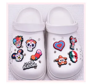 Detailed view of Mexican Day of the Dead themed PVC shoe charms on white clogs.