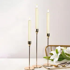 Set of three gold metal candle holders with white LED taper candles on dining table
