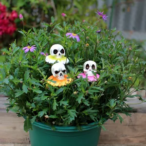Set mit drei Totenkopf-Blumensteckern aus Harz zur Dekoration einer grünen Topfpflanze.