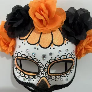 Detail of a Day of the Dead mask with vibrant orange and black silk flowers and gems.