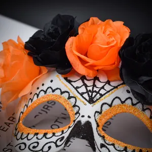 Gros plan d'un masque blanc du Jour des Morts avec des fleurs oranges et noires.