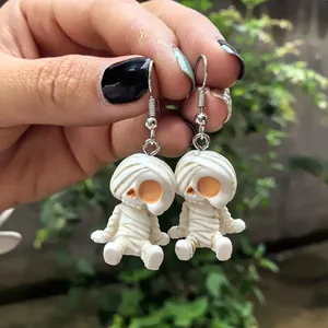 Vue détaillée de boucles d'oreilles pendantes momie squelette Halloween tenues par la main