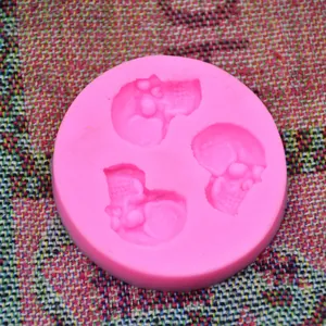 Detail of a pink silicone mold with three skull cavities for fondant or gypsum.